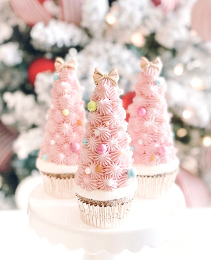 three cupcakes decorated with pink frosting and bows on top of a white cake plate