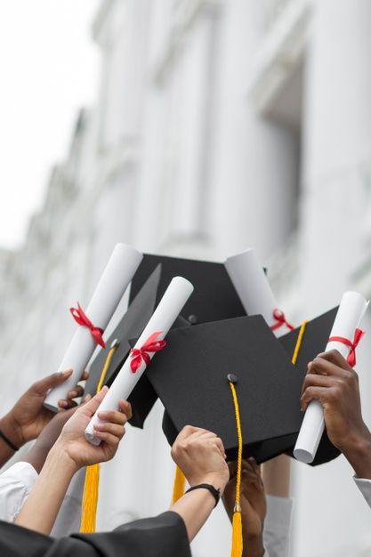 people holding up graduation caps and diplomas in front of a building