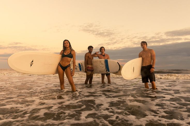 four people are standing on the beach with surfboards in their hands and one is holding a surfboard