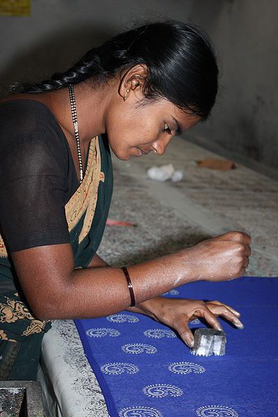 a woman sitting on the floor using a mouse to work on a piece of fabric