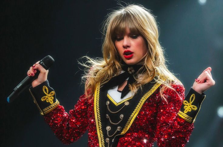 taylor swift performing on stage with microphone in her hand and red sequins around her body