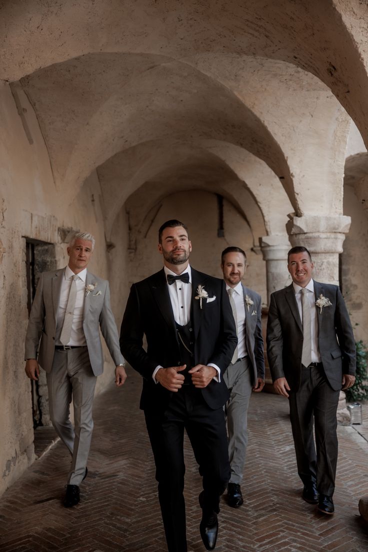 three men in tuxedos are walking through an alley way with one man wearing a suit