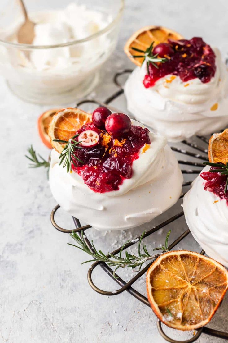 three desserts with cranberry sauce, orange slices and whipped cream on a cooling rack