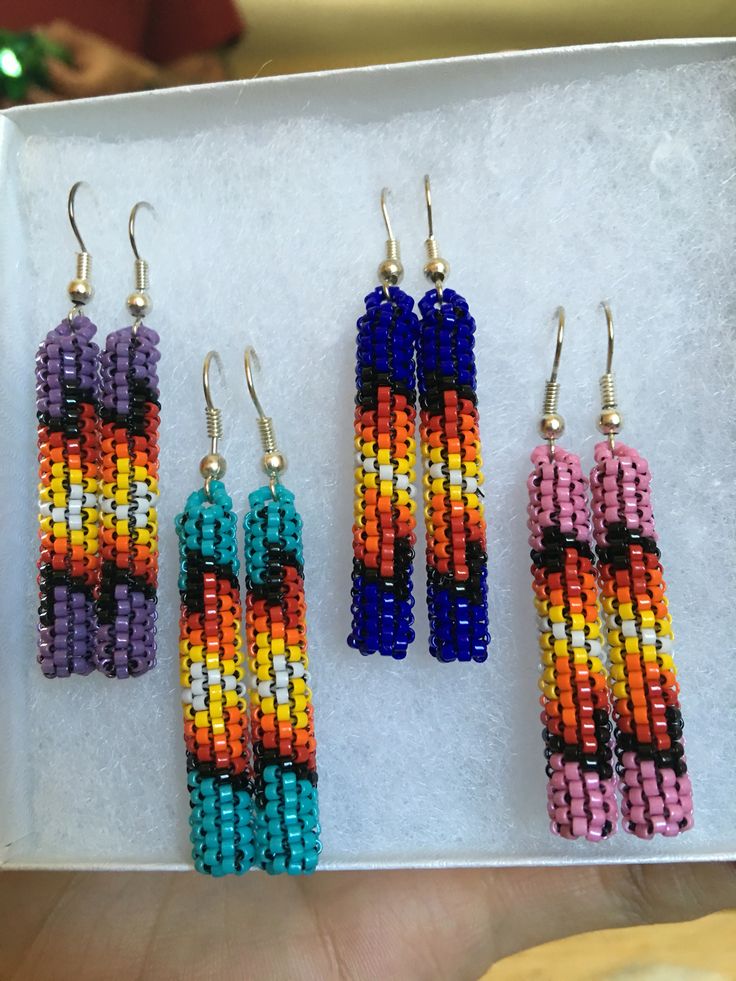 three pairs of beaded earrings are displayed on a white tray in front of other beads