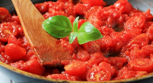 a wooden spoon in a pan filled with tomato sauce and basil leaves on the side