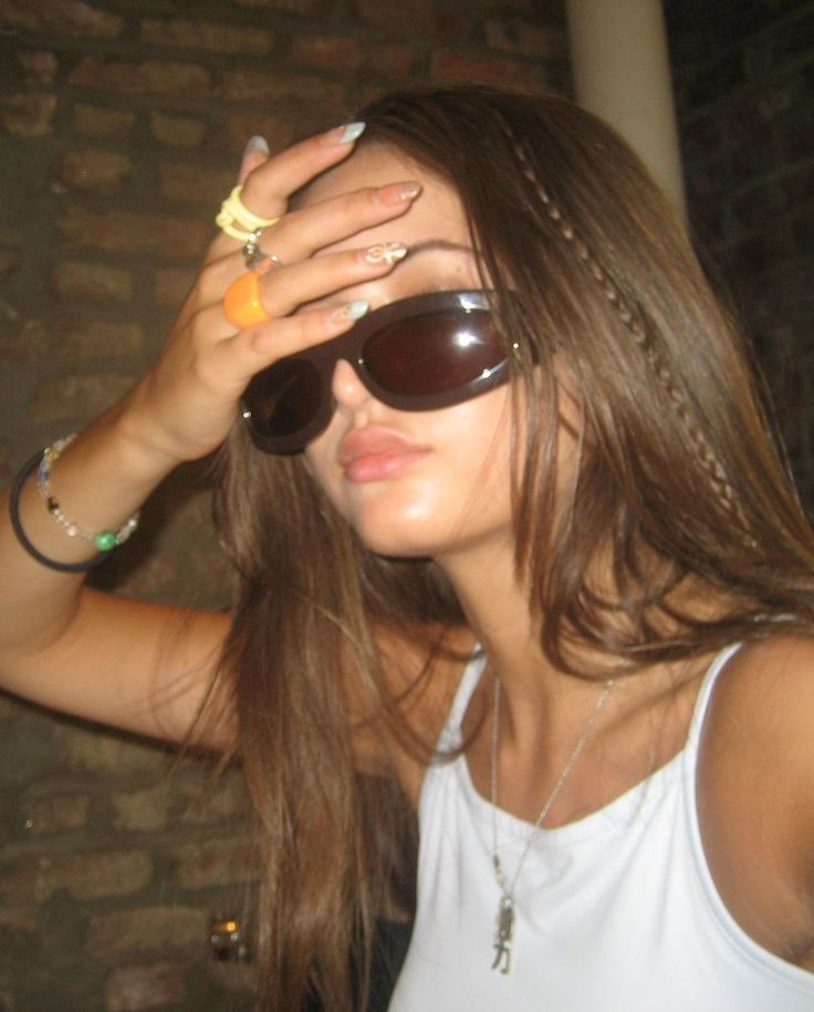 a young woman wearing sunglasses and holding her hand to her face with one eye open