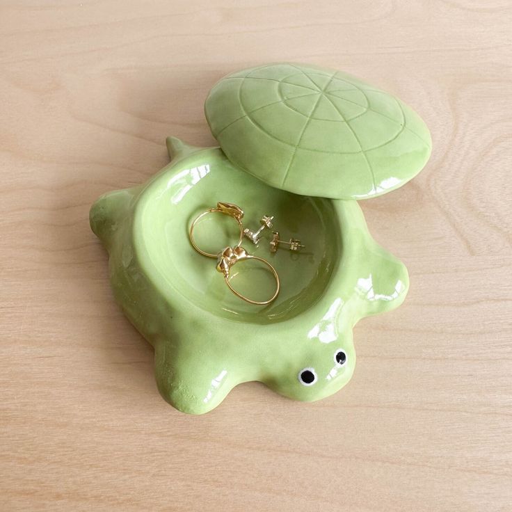 a ceramic turtle with two rings in it's shell on top of a wooden table