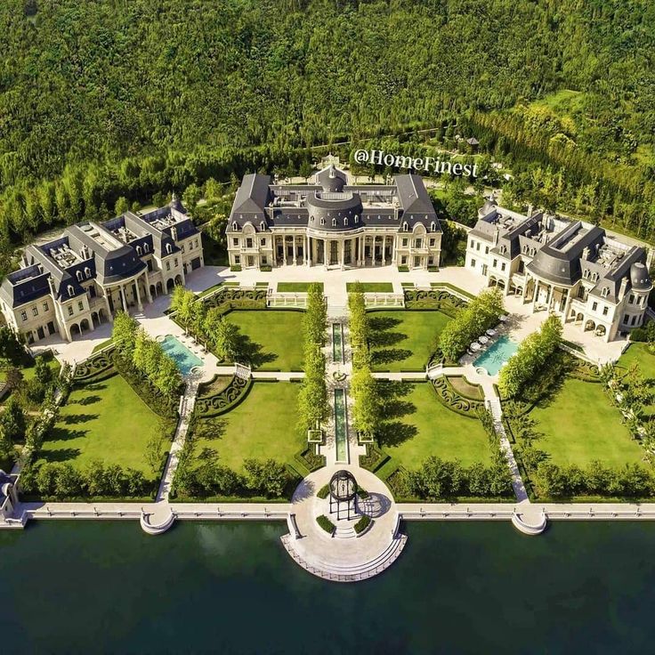 an aerial view of a large mansion on the water's edge, surrounded by lush green trees