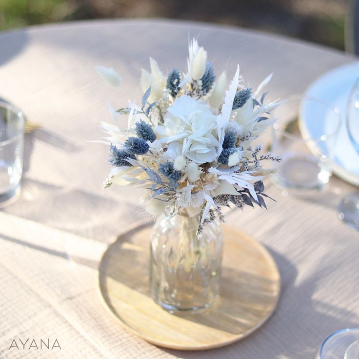 a vase filled with white and blue flowers on top of a wooden table covered in plates