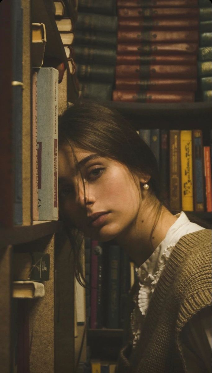 a woman leaning against a book shelf in front of books