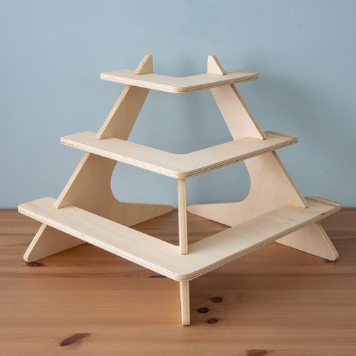 a three tiered wooden shelf sitting on top of a wooden floor next to a blue wall