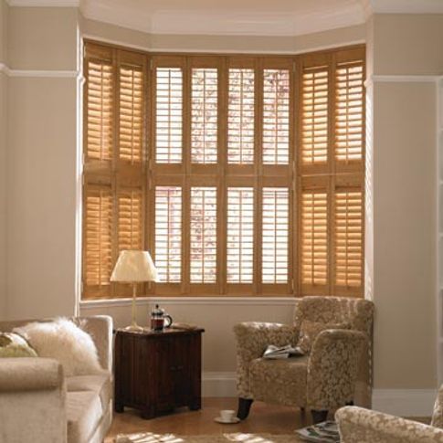 a living room filled with furniture and windows covered in wooden shutters, next to a lamp