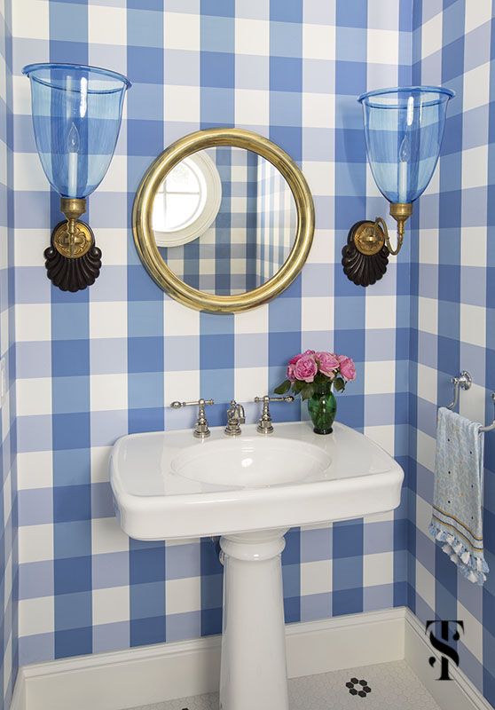 a bathroom with blue and white checkered wallpaper, gold framed mirror and pedestal sink