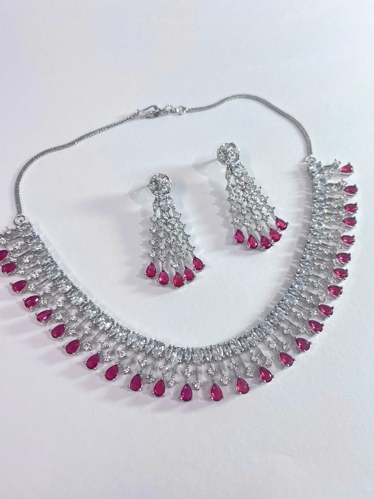 Gorgeous fine quality faux ruby pink color stone with CZ stones  studded in white gold rhodium plating with CZ high quality stones Comes with matching earrings. AAA quality cubic zirconia used. Highest quality and craftsmanship Necklace Fitting is adjustable comes with silver plated back metal chain Earrings Closure: Pushback Necklace Closure: Hook Ruby Jewelry With Diamond Accents For Party, Silver American Diamond Jewelry With Stones, Ruby Drop Jewelry For Anniversary, Pink Ruby Necklace For Formal Occasions, Elegant Pink Hand Set Jewelry Sets, Formal Ruby Drop Jewelry, Pink Crystal Jewelry Sets For Formal Occasions, Dazzling Red American Diamond Jewelry, Formal Pink Crystal Jewelry Sets