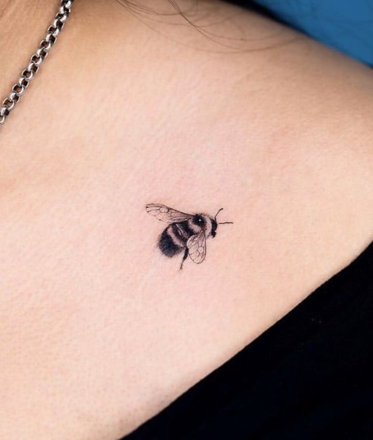 a small black and white bee tattoo on the back of a woman's shoulder