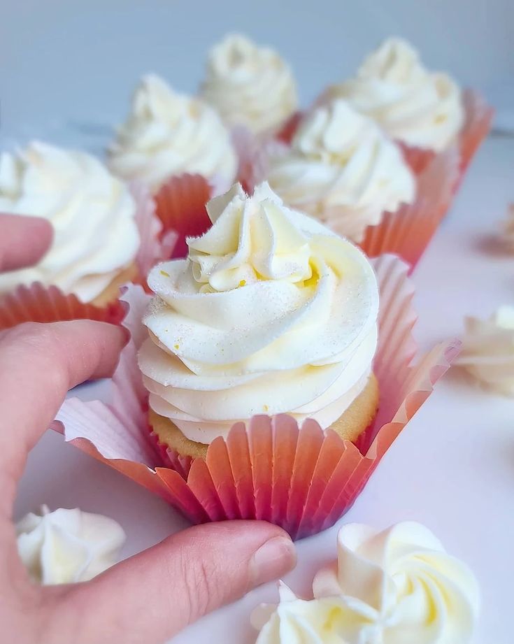 a hand is reaching for some cupcakes with white frosting on them and sprinkled with icing