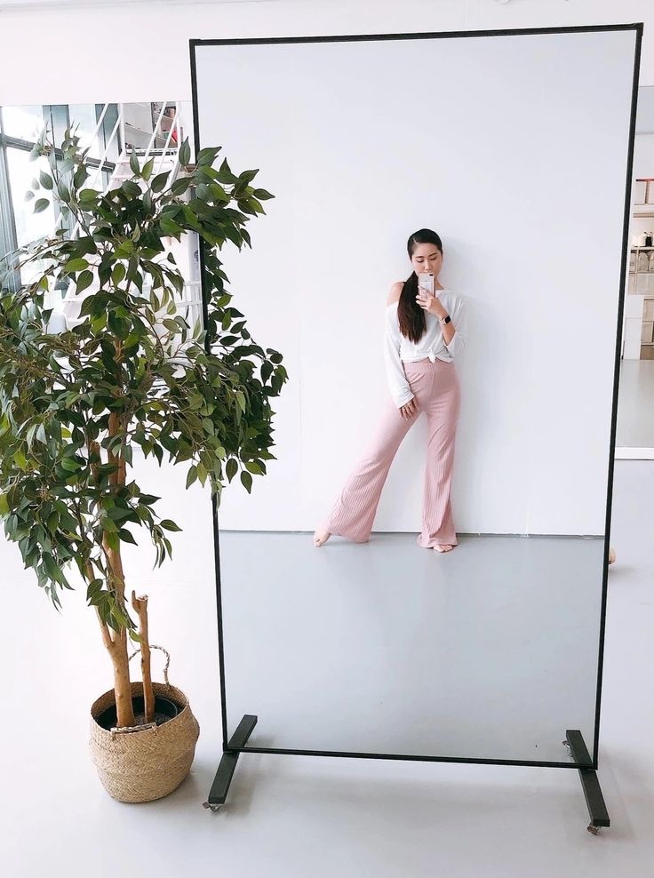 a woman in pink pants leaning against a white wall next to a potted plant