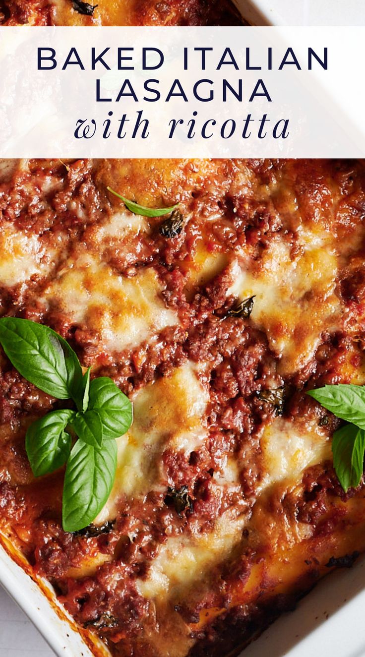 baked italian lasagna with ricotta in a white casserole dish and basil leaves on top