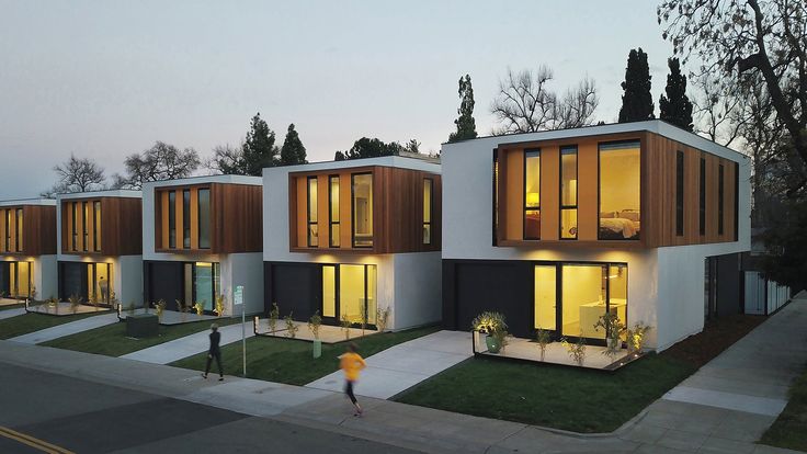 three story house with multiple windows and lights on the front, two people walking by