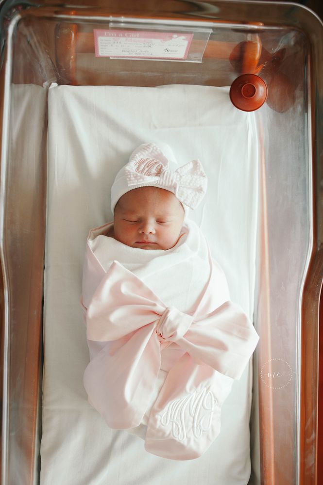 a baby in a crib with a pink blanket on it's head and bow around its neck