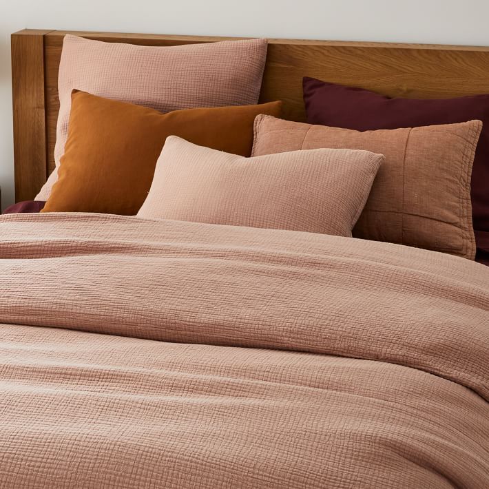 a bed with pink sheets and brown pillows