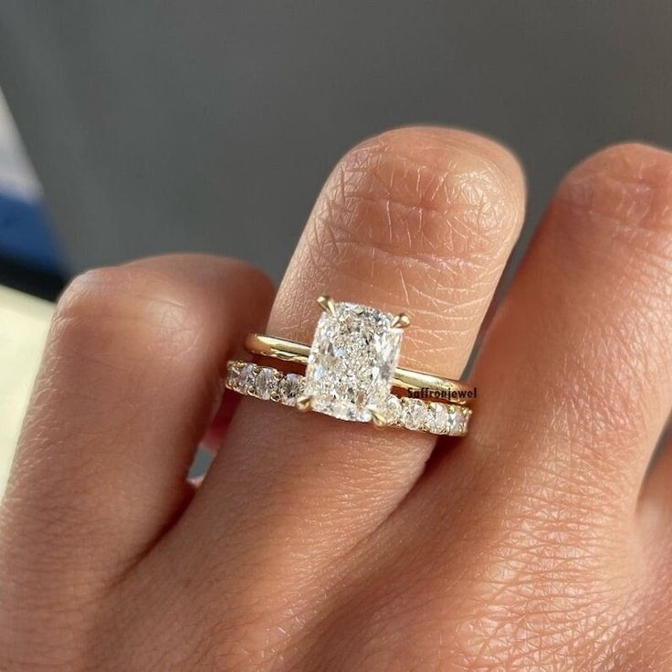 a woman's hand with a diamond ring on top of her finger and the other hand holding an engagement ring