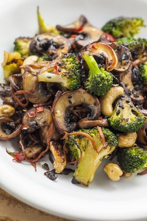 broccoli, mushrooms and other vegetables on a white plate sitting on a wooden table