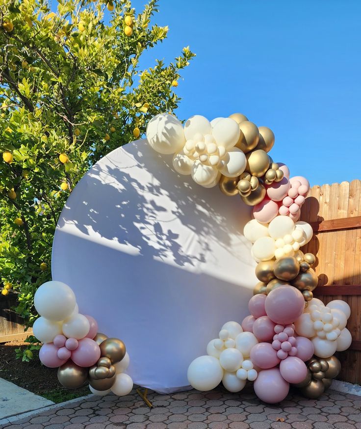 a white and gold balloon arch in front of a wooden fence