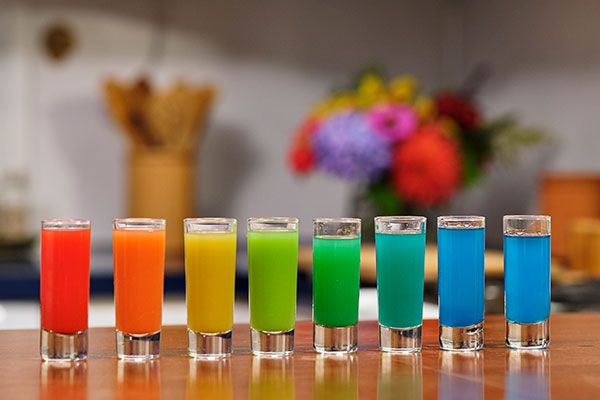 seven shot glasses filled with different colored drinks