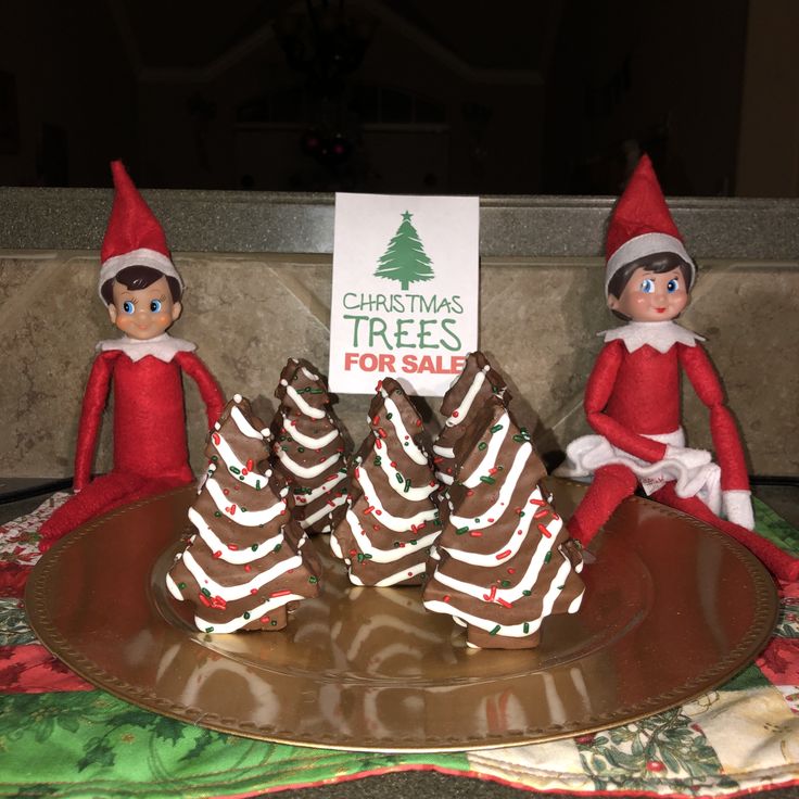 three elfs sitting on top of a table with christmas trees for sale sign in front of them