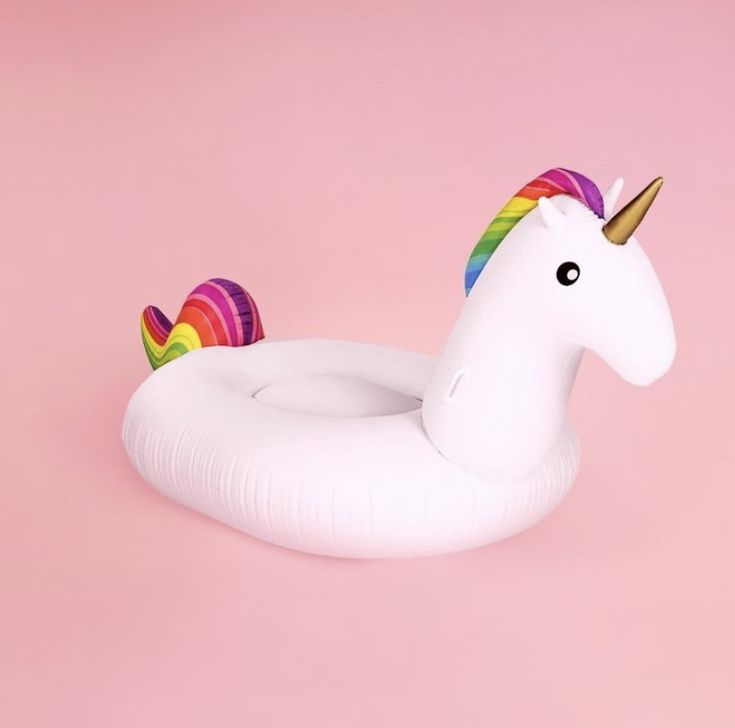 an inflatable unicorn float on a pink background with a rainbow horn and tail