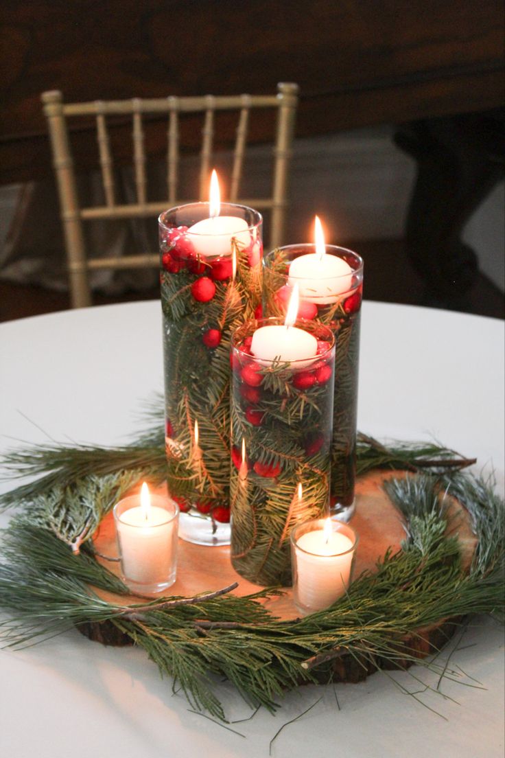 candles are arranged in glass vases on a tray with evergreen branches and red berries