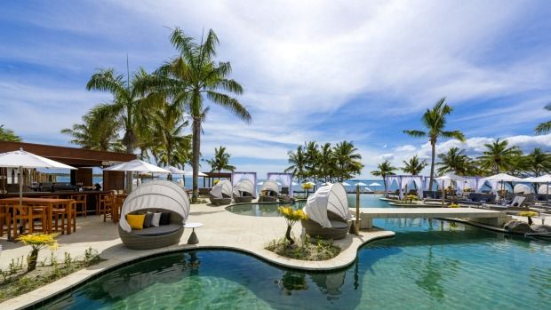 an outdoor swimming pool with lounge chairs and umbrellas next to the ocean in front of palm trees