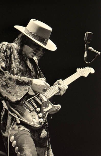 a man in a fedora playing an electric guitar