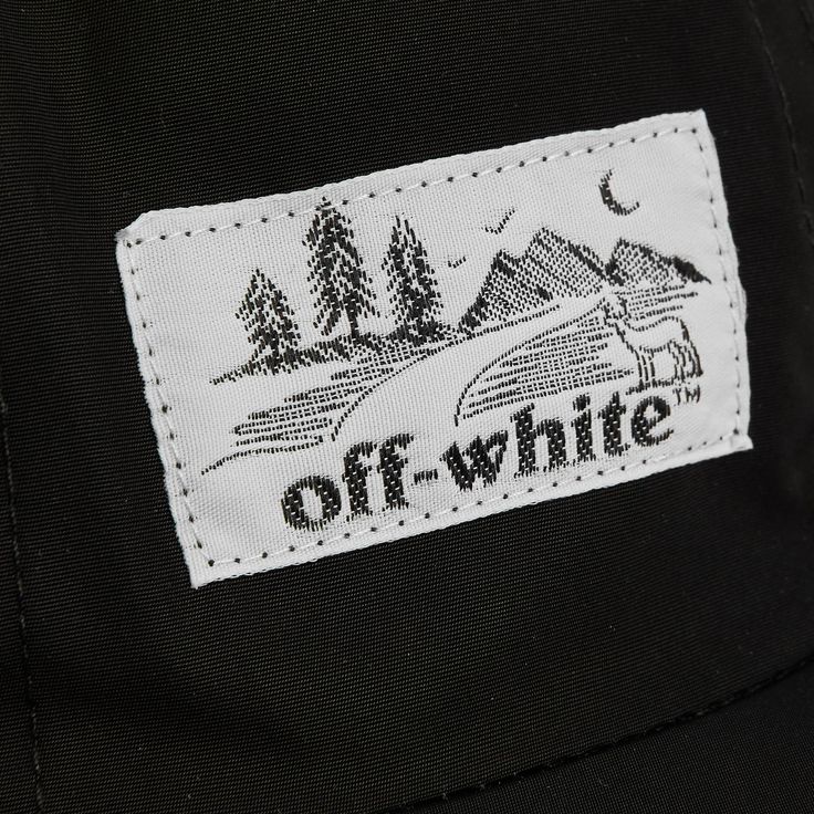 the off - white patch is on top of a black hat with trees and mountains in the background