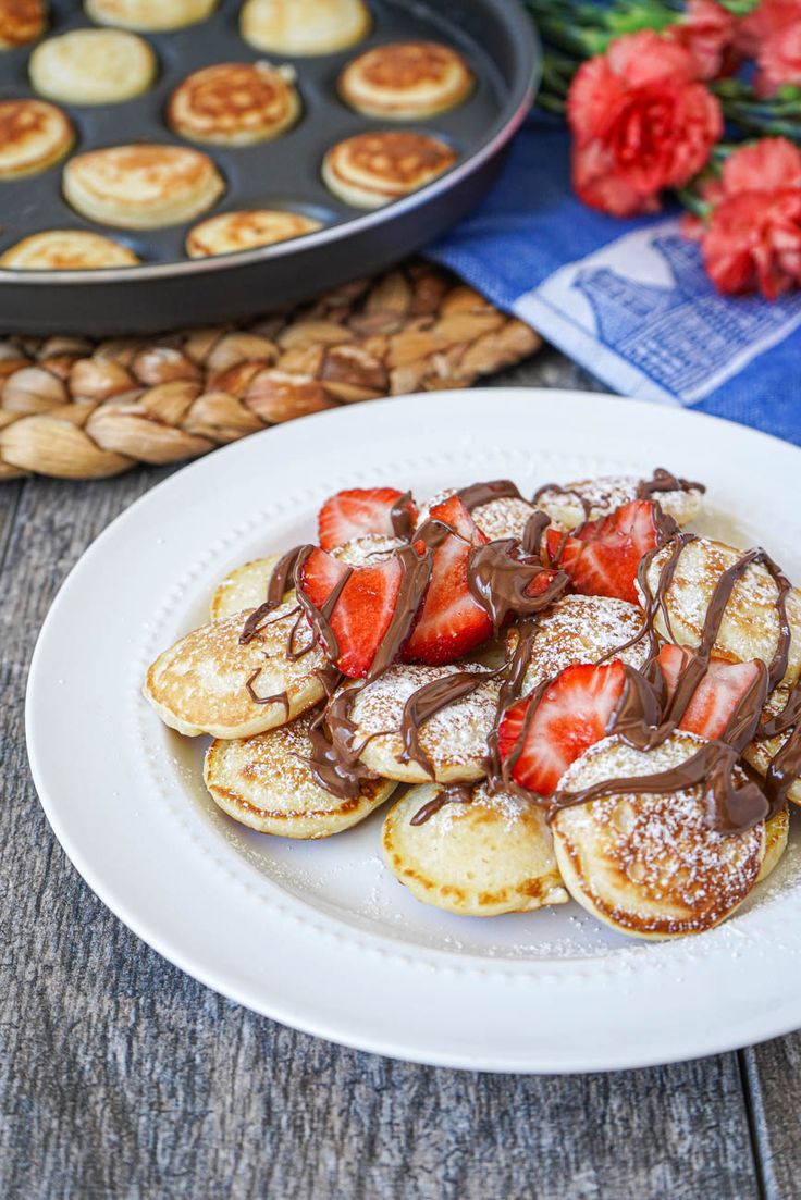 a white plate topped with pancakes covered in powdered sugar and strawberries next to a muffin tin