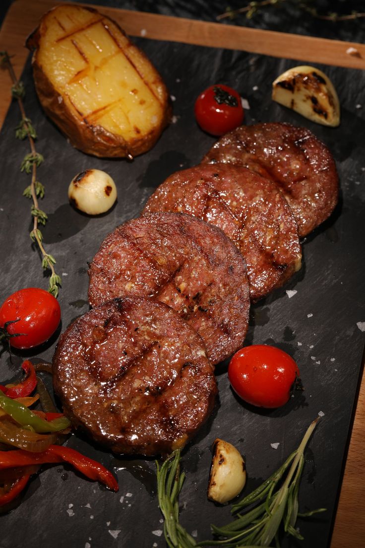 steak, potatoes and tomatoes on a slate platter with garnishes in the background