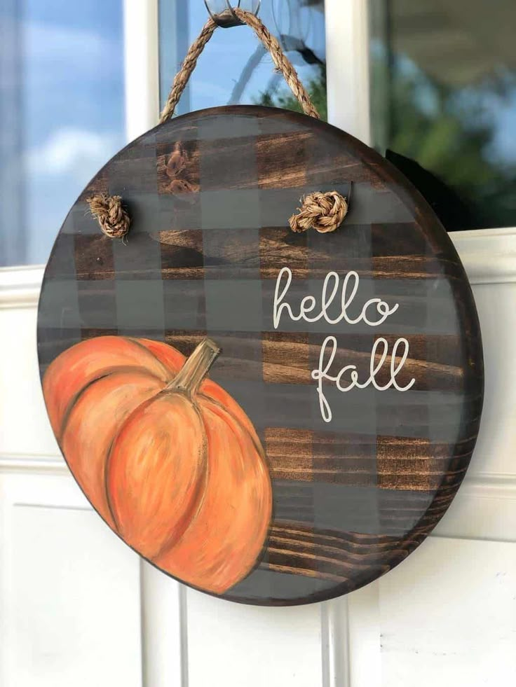 a wooden sign that says hello fall hanging from the side of a door with a pumpkin painted on it