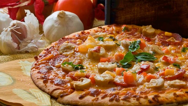 a pizza sitting on top of a wooden cutting board next to garlic and pepperoni