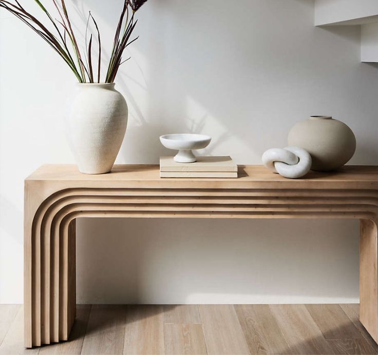 two white vases sitting on top of a wooden table next to a book shelf