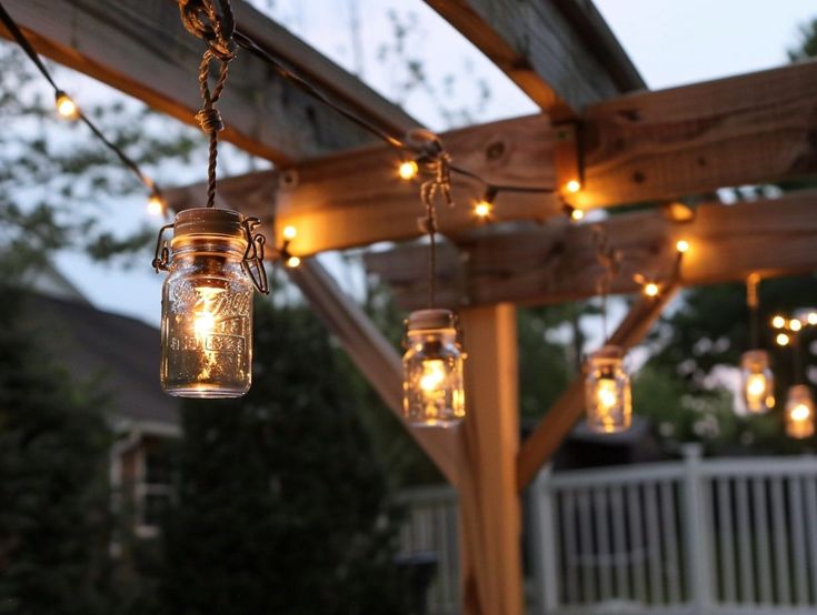 mason jar lights hanging from a wooden pergolan with string lights on the outside