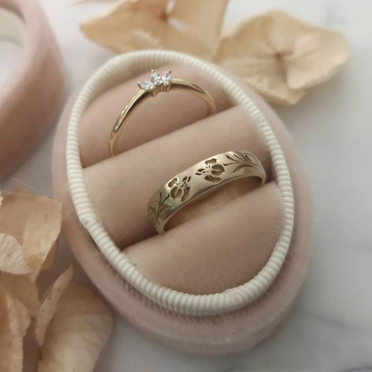 two wedding rings in a ring box with flowers on the ground next to each other