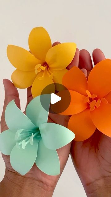 two hands holding three paper flowers in each other's palm, with the video below them