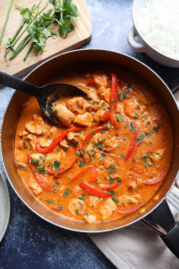 a skillet filled with chicken and vegetables on top of a blue countertop next to rice