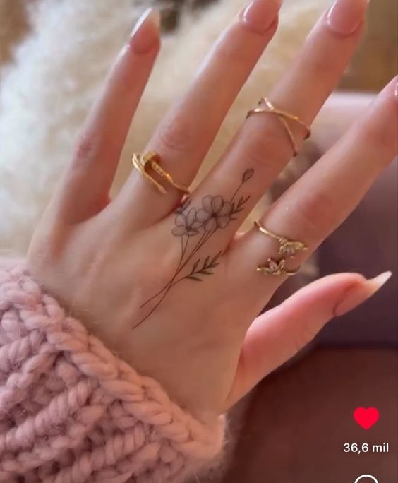 a woman's hand with three rings on it and flowers tattooed on the middle finger