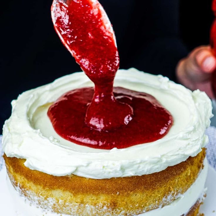 a cake with white frosting and a strawberry on top is being drizzled with red sauce