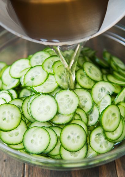 cucumber slices being cut into small pieces in a bowl with a metal strainer