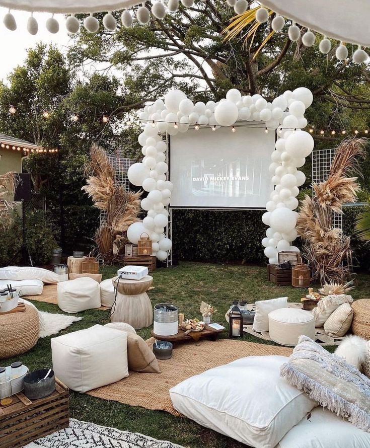 an outdoor movie is set up in the backyard with balloons and pillows on the grass