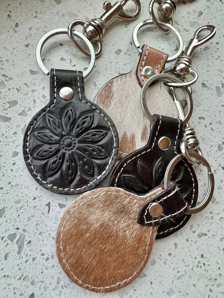 three leather keychains with different designs on them