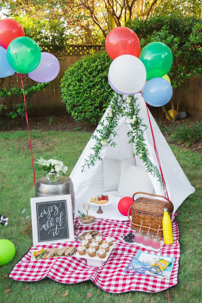 a teepee tent with balloons, cake and cupcakes on the grass in front of it